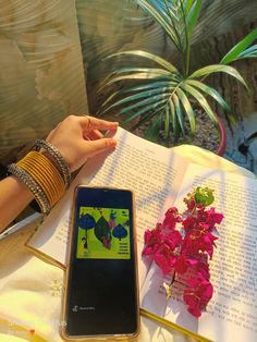 a person is reading a book and holding a cell phone in front of them on a table