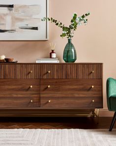 a wooden dresser with two green chairs next to it and a painting on the wall