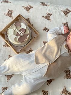 a baby laying on top of a bed next to a cake