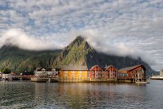 some houses are on the water and mountains in the background with clouds rolling over them