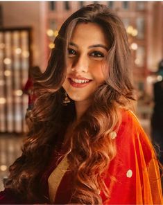 a woman with long hair wearing an orange and yellow sari smiling at the camera