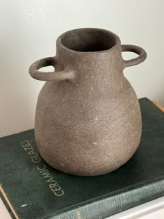 a gray vase sitting on top of a green book