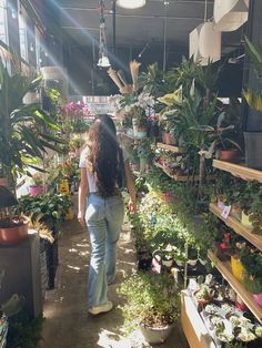 a woman walking through a flower shop filled with potted plants