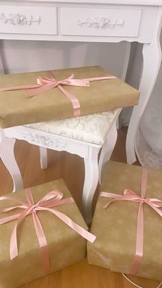 three wrapped presents sitting on top of a wooden floor next to a white table and chair