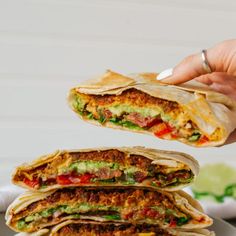 a hand holding a tortilla with meat and vegetables