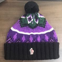 a purple and black knitted hat sitting on top of a wooden table next to a laptop computer