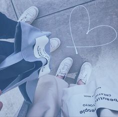 someone is drawing a heart on the ground with white shoes and blue bag next to them