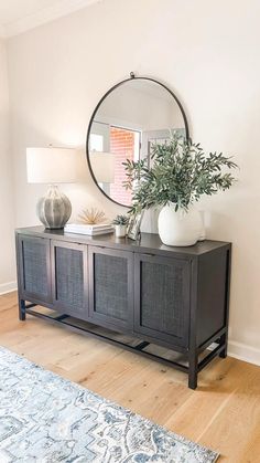 a large round mirror sitting on top of a wooden cabinet next to a vase filled with plants