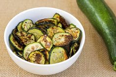 a white bowl filled with cooked zucchini next to a cucumber