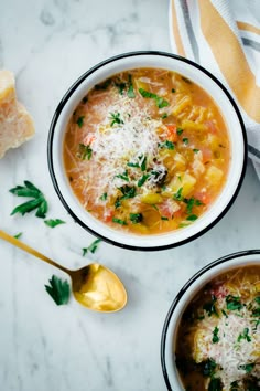 two bowls of soup with parmesan cheese on top and bread in the background