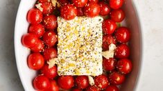 a white bowl filled with lots of tomatoes and topped with a square piece of cheese