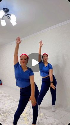 two women in blue shirts and red headbands are doing yoga exercises with their hands up