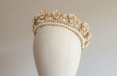 a white mannequin wearing a gold tiara with pearls and flowers on it