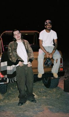 two men sitting on the back of a pick up truck in the desert at night