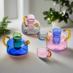 several different colored glass teapots and cups on a table