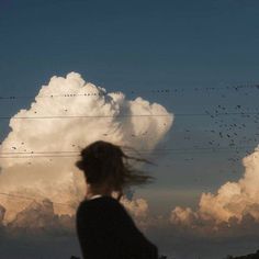 a woman standing in front of a large cloud with birds flying over her and power lines