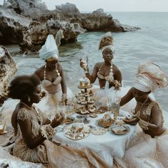 four women dressed in traditional african clothing sitting at a table with desserts on it