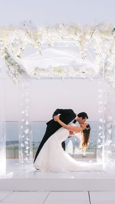 a bride and groom kissing in front of an arch with flowers on the floor at their wedding