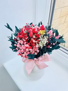 a white vase filled with lots of red and pink flowers on top of a window sill