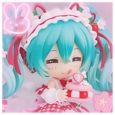 an anime doll with blue hair holding a pink cupcake in her hand and smiling at the camera