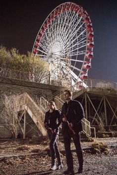 two people standing next to each other in front of a ferris wheel