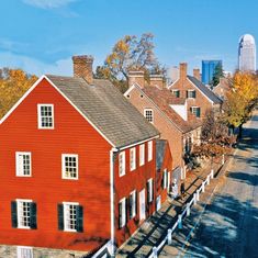 a red house with white shutters in front of a cityscape on a sunny day