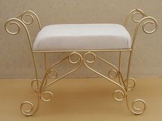 a small gold metal bench with a white cushion on it's seat and back