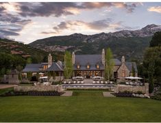 a large stone house surrounded by lush green grass and trees with mountains in the background