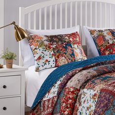 a bed with colorful quilts and pillows on it in a white room next to a night stand