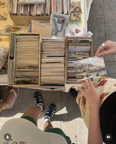 two people sitting at a table with many books and magazines on it, one person is reading