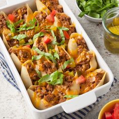 a casserole dish filled with pasta, meat and veggies next to salad