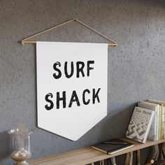 a surf shack sign hanging on the wall above a shelf with books and other items