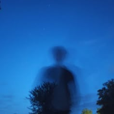 a blurry image of a person standing in the dark with trees and bushes behind him