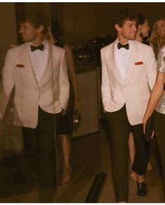 two men in tuxedos are looking at each other through a glass door while others look on