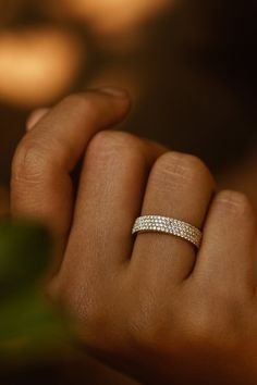 a woman's hand with a diamond ring on her left hand and a green plant in the background