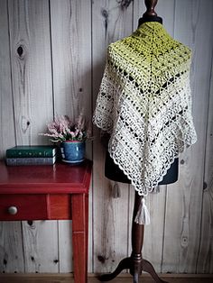 a yellow and white crocheted shawl sitting on top of a wooden table