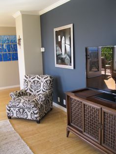 a living room with a chair, television and painting on the wall in it's corner