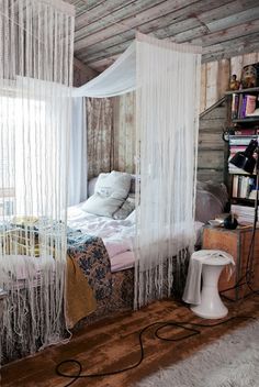 a bedroom with a bed, rugs and white curtains hanging from the ceiling in front of a window