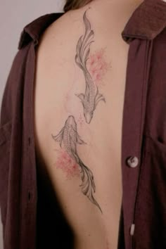 a woman's back with a fish tattoo on her left shoulder and pink flowers in the background