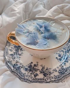 a blue and white cup with flowers in it on a saucer next to a bed