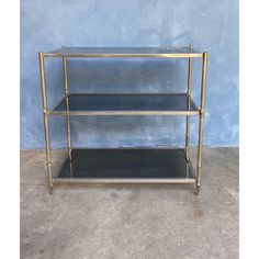 a three - tiered brass and glass shelf with black shelves against a blue wall