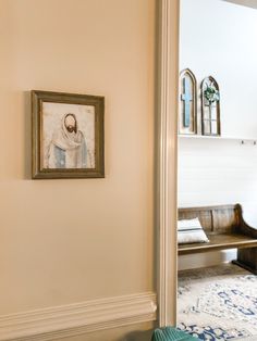 a painting hangs on the wall next to a bench and mirror in a room with white walls