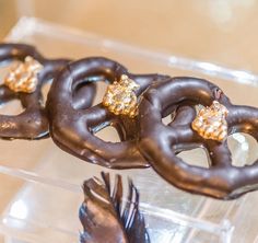 three chocolate pretzels with gold decorations on them sitting in a plastic container next to a bird