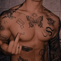 a shirtless man with tattoos on his chest pointing to the side while standing in front of a tiled wall