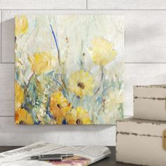 a painting is hanging on the wall next to some books and a vase with yellow flowers