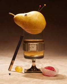 a pear sitting on top of a glass next to a pencil and an object in the shape of a clock