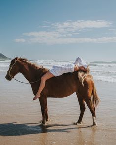 a woman riding on the back of a brown horse near the ocean's edge