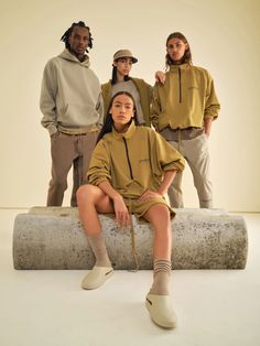 four people standing in front of a white wall wearing hoodies and sweatpants, all looking at the camera