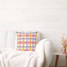 a white couch sitting next to a table with a vase on it and a plaid pillow