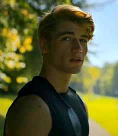 a young man standing in front of a tree looking at the camera while wearing a black shirt